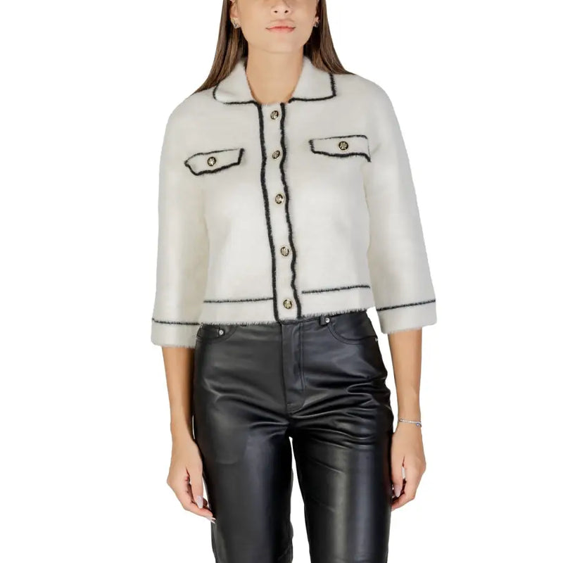 Woman wearing a white cropped cardigan with black trim over black leather pants