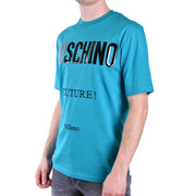 Türkisfarbene Moschino-Herren t-shirt mit markanter schwarzer und silberner Schrift, die die Wörter Moschino Couture und Milano enthält.