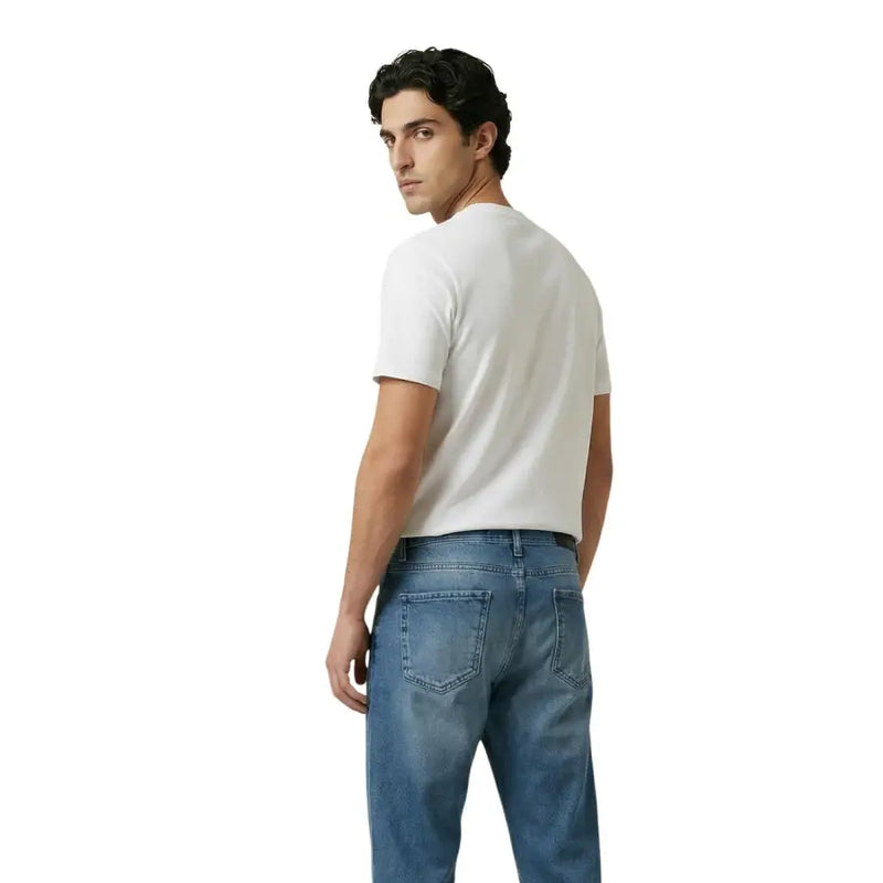 A man wearing a plain white short-sleeved cotton t-shirt and medium-wash blue denim jeans by New Balance