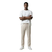 A man wearing only & sons beige drawstring trousers and a white t-shirt showcasing casual men’s pants