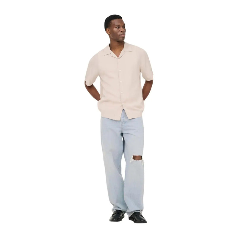 Ein Mann, der only Beigefarbenes Tencel-Herrenhemd mit V-Ausschnitt von and Sons, kombiniert mit hellblauen Jeans mit Rissen
