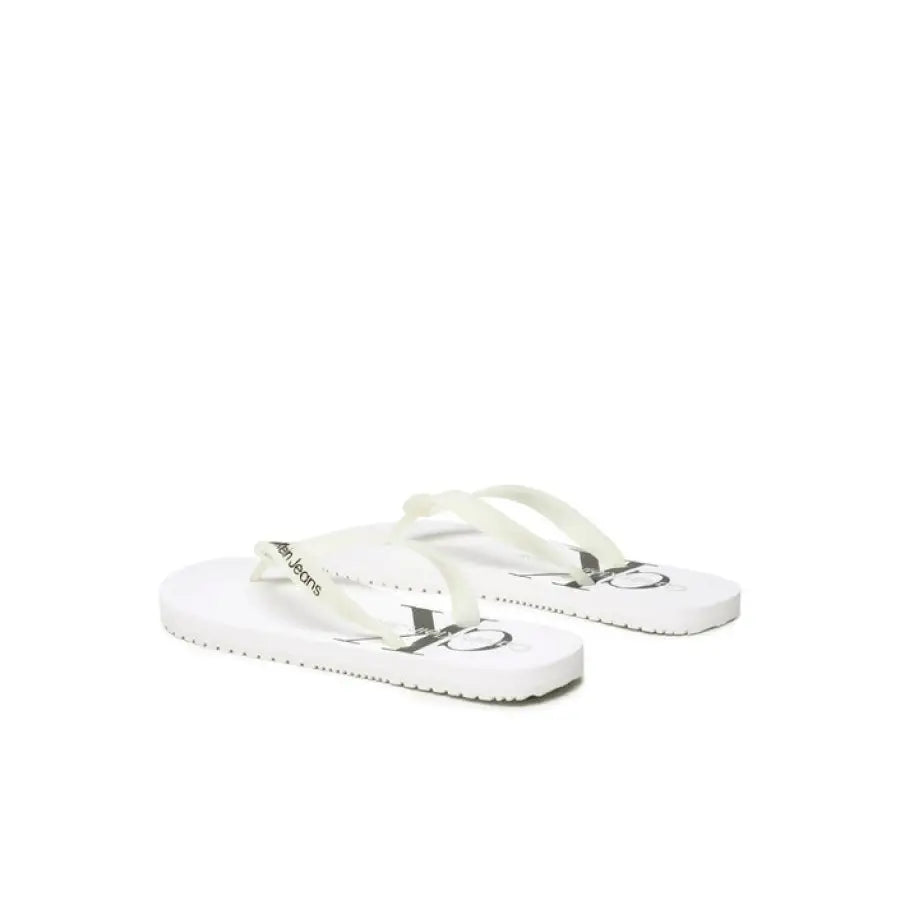 
                      
                        Calvin Klein Jeans men’s white flip flops with silver buckle on display
                      
                    