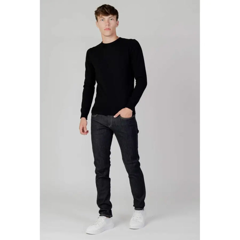 Schwarzer, langärmeliger Rundhalspullover aus weichem Strickmaterial, kombiniert mit blauer, schmal geschnittener Replay Herrenjeans mit Reißverschluss und Knopf (Modell M914Y).