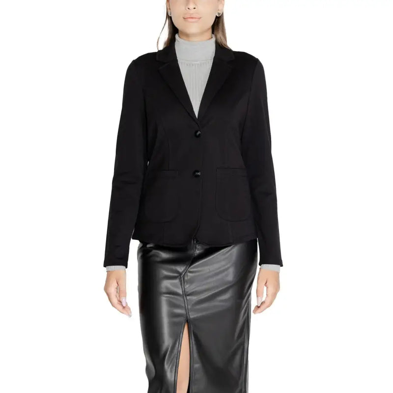 Women wearing black tailored blazer with flap pockets over light grey turtleneck and black faux leather midi skirt