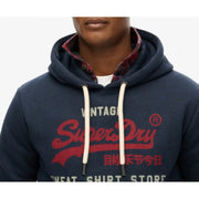 Men’s navy blue Superdry hoodie with red logo and white drawstrings over plaid shirt