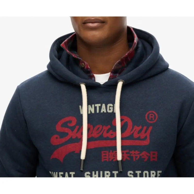 Men’s navy blue Superdry hoodie with red logo and white drawstrings over plaid shirt