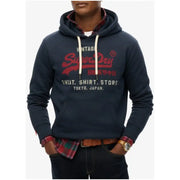Dark blue hooded sweatshirt with Super Dry logo over red plaid shirt and blue jeans