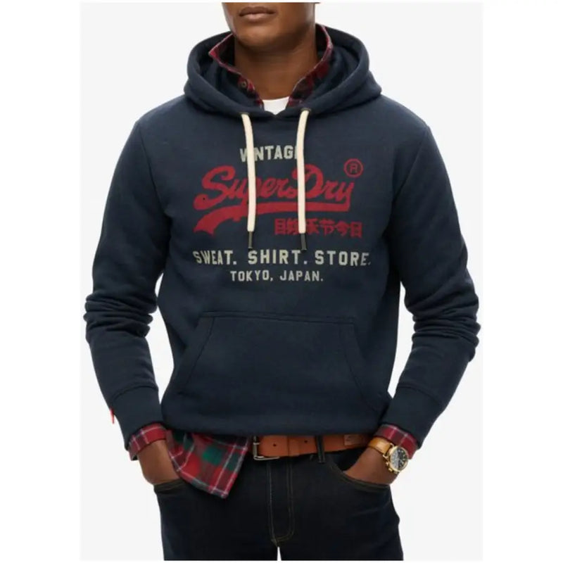 Dark blue hooded sweatshirt with Super Dry logo over red plaid shirt and blue jeans