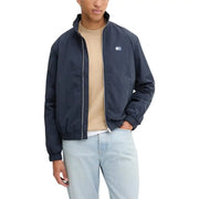 Men’s navy blue windbreaker jacket with white zipper over tan T-shirt and light blue jeans