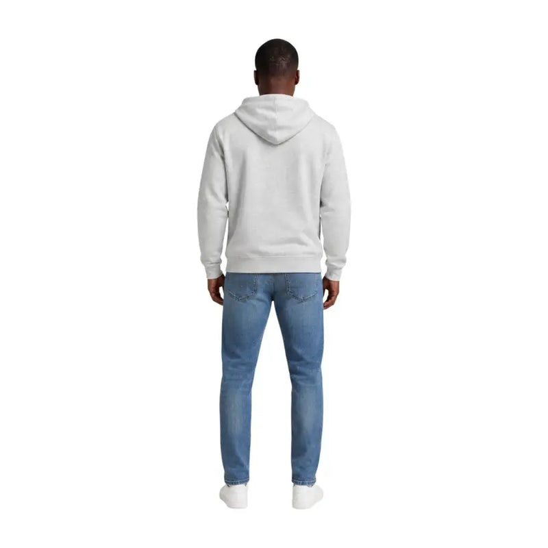 A man wearing a light gray hooded Tommy Hilfiger sweatshirt paired with blue denim jeans for men