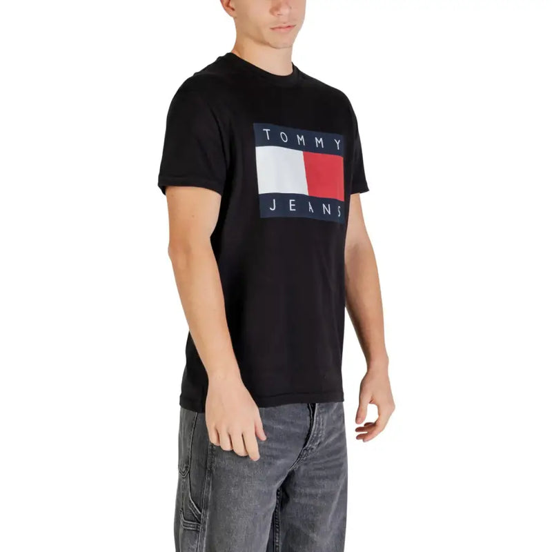 Noir Tommy Hilfiger Jeans t-shirt présentant un logo rectangulaire audacieux avec des rayures blanches et rouges bordées de texte bleu marine