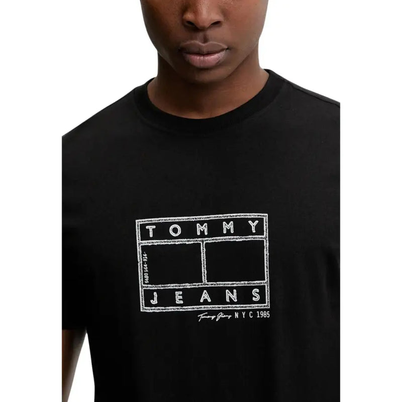 Noir Tommy Hilfiger jeans hommes t-shirt avec le logo Tommy Jeans NYC 1985 en blanc craie sur le devant