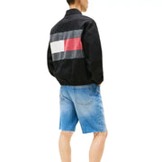 Men’s black windbreaker jacket with large flag design worn with distressed blue denim shorts