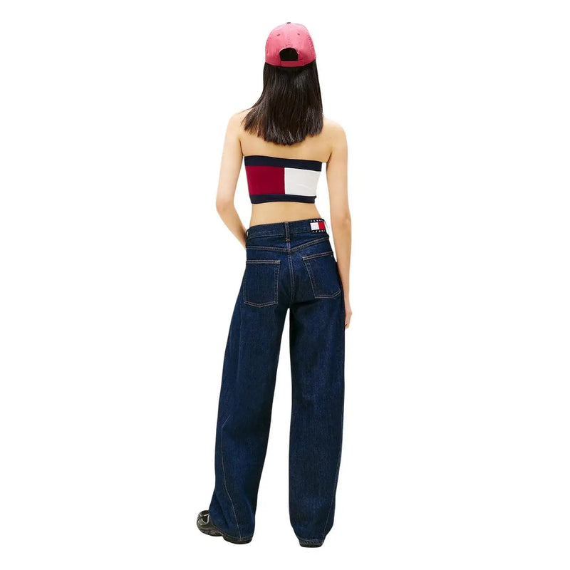 A woman wearing dark blue wide-leg organic cotton tommy hilfiger jeans with logo on back waistband and a pink cap