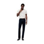 Ein Mann in einem strahlend weißen Tommy Hilfiger Poloshirt aus Baumwolle kombiniert mit einer blauen Baumwollhose im Denton-Schnitt.