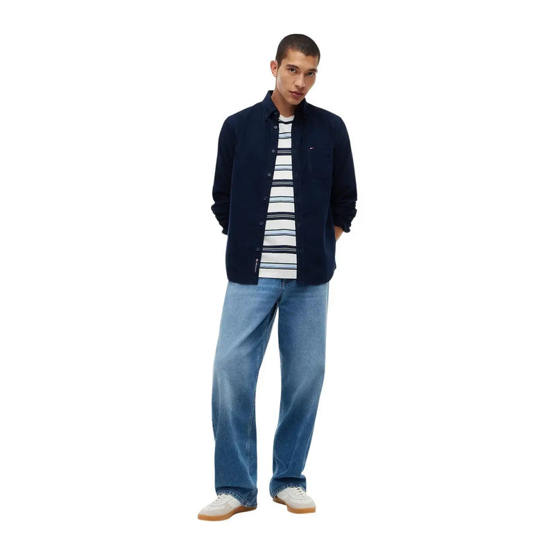 Tommy Hilfiger Herren-Jeanshemd aus blauer Baumwolle, lässig kombiniert mit einem dunkelblauen Button-Down-Hemd und einem gestreiften T-Shirt über hellen Jeans.