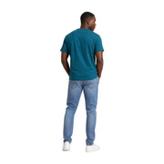 A man wears a teal green organic cotton short-sleeved t shirt paired with light-wash denim jeans by Tommy Hilfiger