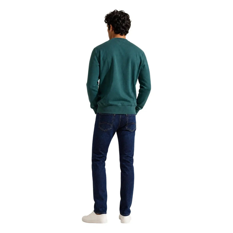 Ein Mann, der einen Tommy Hilfiger Herren-Sweatshirt aus grünem Baumwollfleece mit marineblauen Jeans für einen lässigen Look