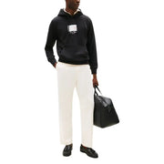 Schwarze Leder-Reisetasche mit einzelner Schnalle vorne und top Griffe kombiniert mit einem schwarzen Tommy Hilfiger Herren-Hoodie aus Bio-Baumwolle