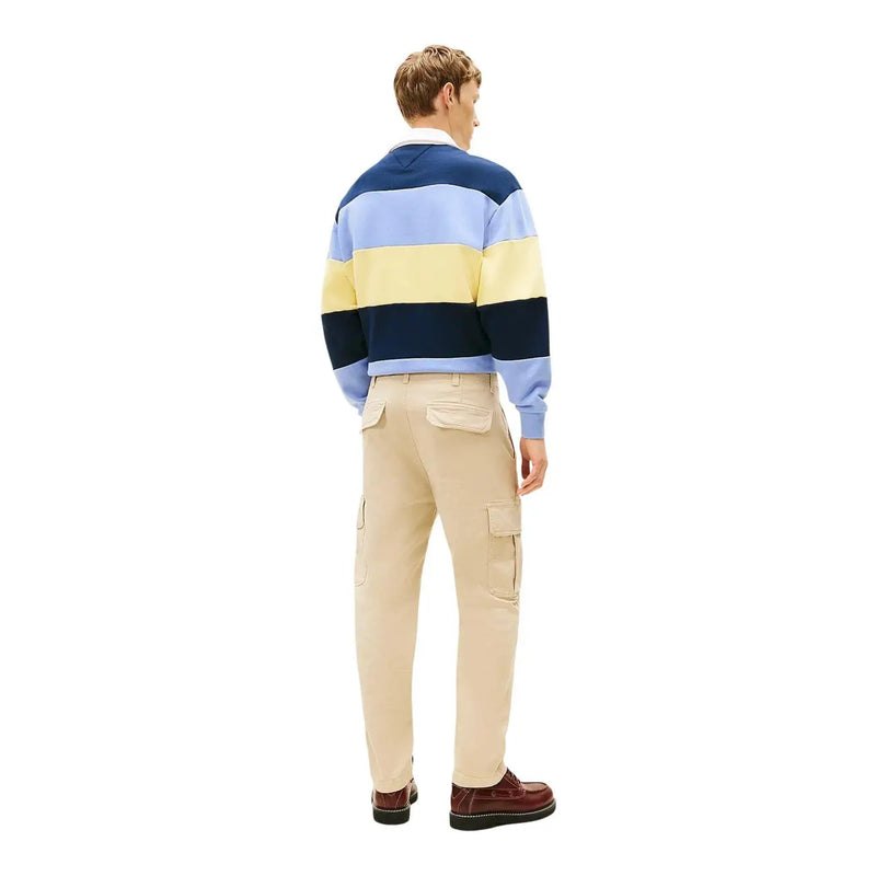 A man wearing a navy light blue and yellow striped rugby sweater paired with Tommy Hilfiger jeans trousers
