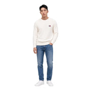 Ein cremefarbener Tommy Hilfiger Pullover aus Bio-Baumwolle mit Rundhalsausschnitt und kleinem, gesticktem Logo auf der linken Brust.