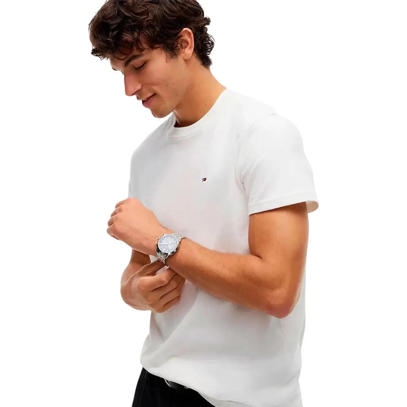 Silberfarbene Armbanduhr mit rundem Zifferblatt und Metallarmband, getragen am Handgelenk, kombiniert mit einem weißen T-Shirt aus Bio-Baumwolle von Tommy Hilfiger für Herren.