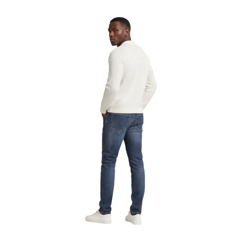A man wearing tommy hilfiger men scanton slim blue jeans cotton paired with a cream-colored long-sleeved knit sweater