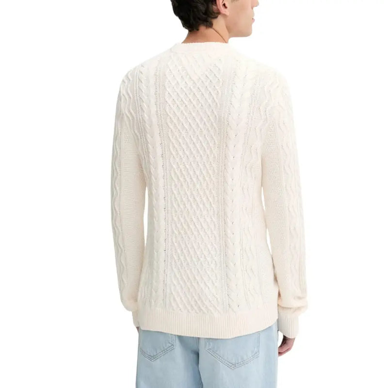 Cream cable knit sweater with light wash denim jeans and a round neckline.