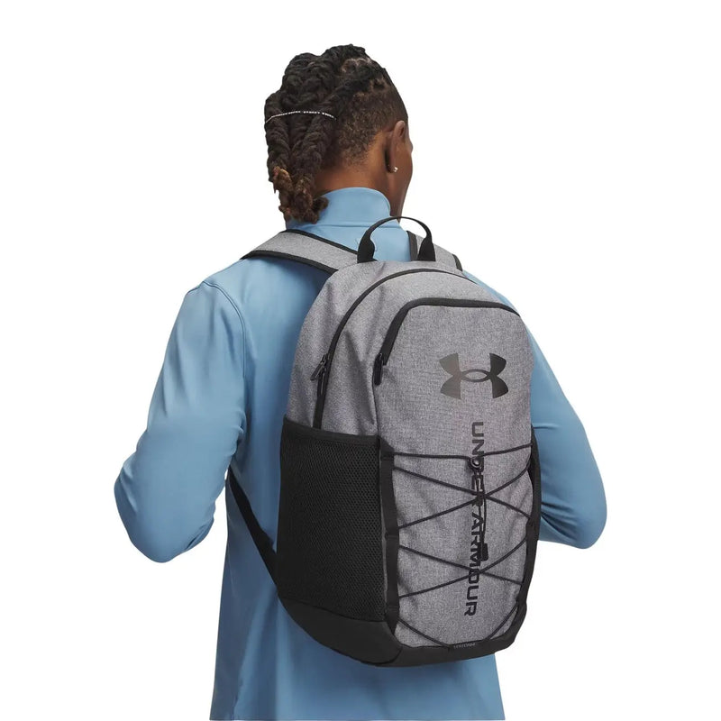 Under armour men hustle sport 6.0 backpack in grey with textured fabric, mesh side pocket, and crisscrossed webbing straps