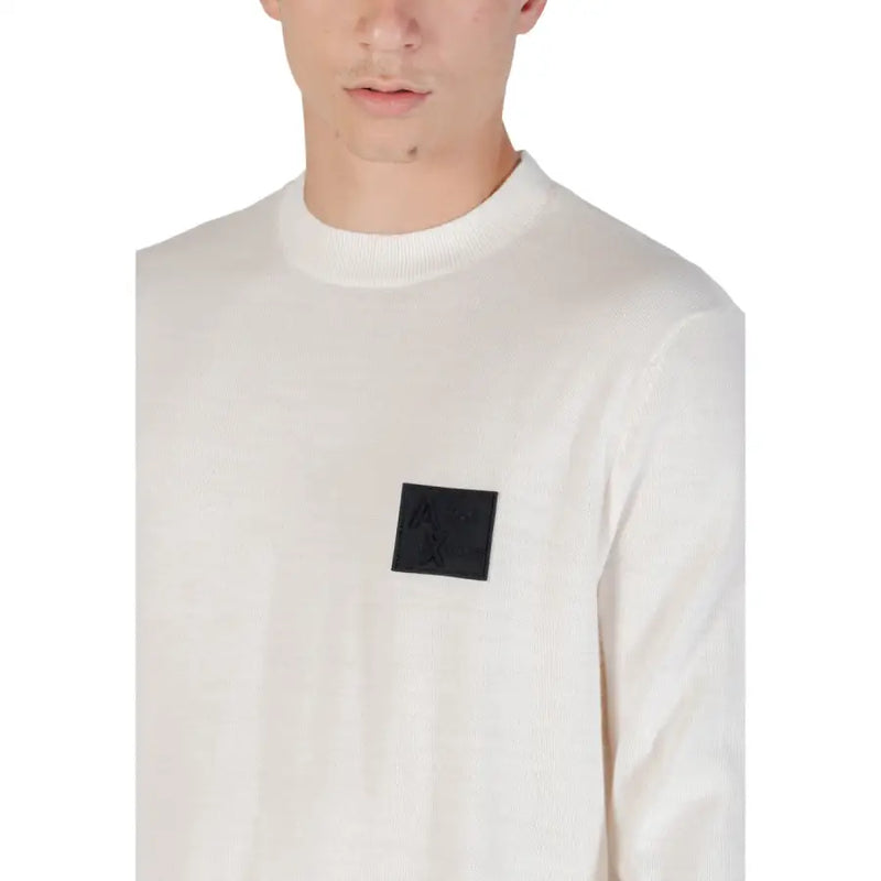 White long sleeved crewneck sweater in cream ribbed knit with a black square patch on the chest