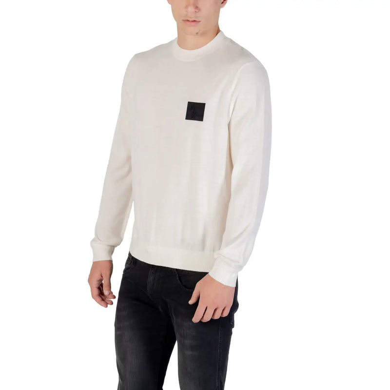 White long sleeved crewneck sweater in cream color with a black square patch on the left chest