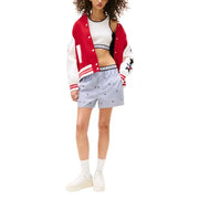 Woman in red and white letterman jacket, white crop top, and light blue patterned shorts