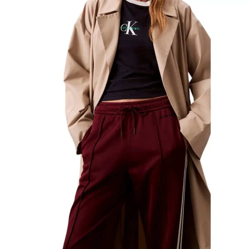 Woman in tan trench coat, black CK t-shirt, and Bordeaux lace trousers for women