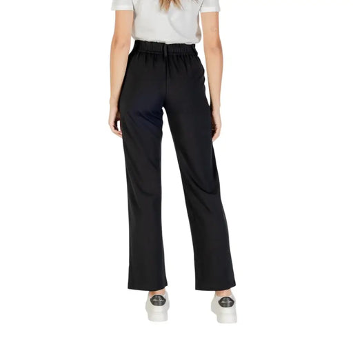 Women wearing black high-waisted paperbag trousers with a white top and sneakers