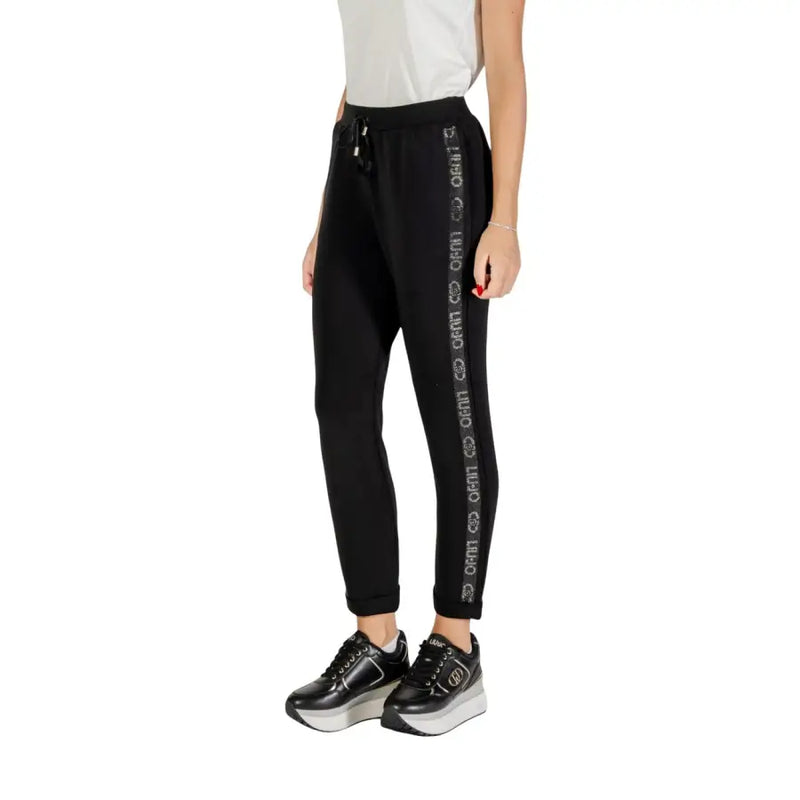 Women’s black track pants with white stripe and repeated text, paired with black platform sneakers