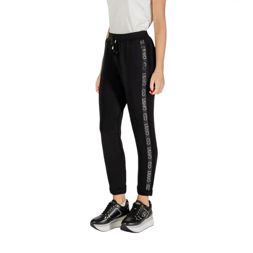 Women’s black track pants with white stripe and repeated text, paired with black platform sneakers